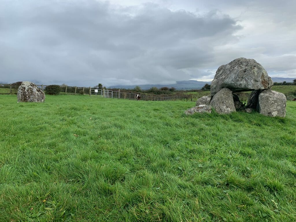 Lush green pasture with neolithic stone structures on the right and left side of the image, grey sky