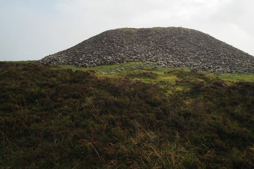 Brown/green brush in the foreground, background a hill of round stones - Knocknarae in Sligo