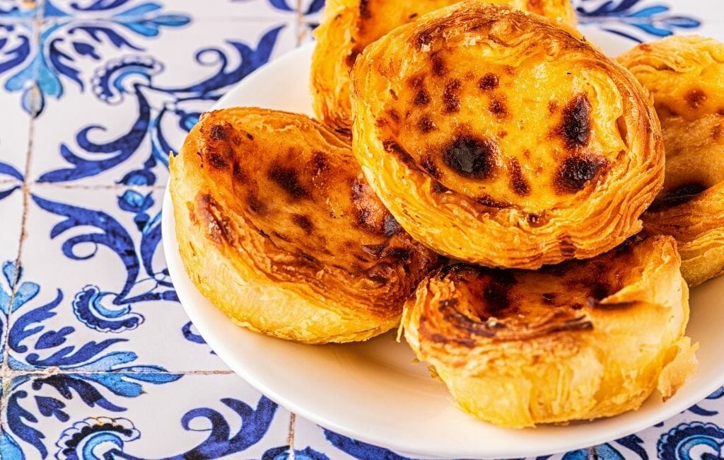 Pastel de Nata on a plate on a surface with blue and white traditional Portuguese tile - Portuguese Dessert - Famous Food of Portugal