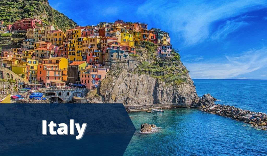 small village perched on steep cliff in cinque terre italy during sunset with blue banner on the bottom left with white text Italy