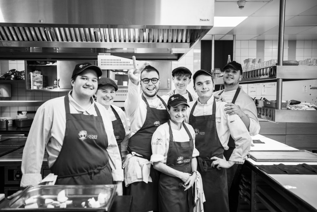 Black and white photo of 7 chefs working in a kitchen posing around chef