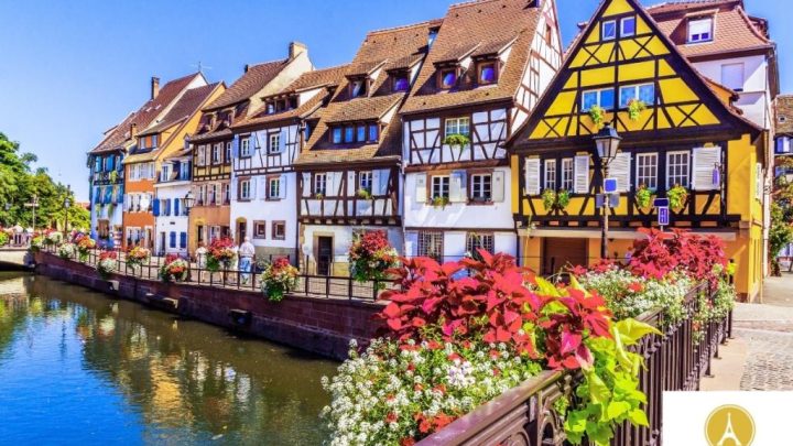 row of colorful half-timbered houses with a small river in front on a sunny summer day