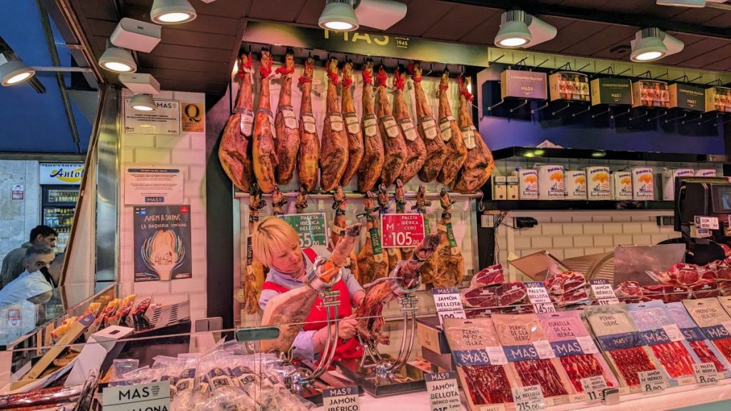 Female shop worker at a shop at La Boqueria market in Barcelona selling ham
