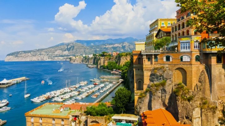 Colorful cliffside buildings overlooking mountain coast and harbor full of boats during summer. Where to stay in Sorrento, Italy.